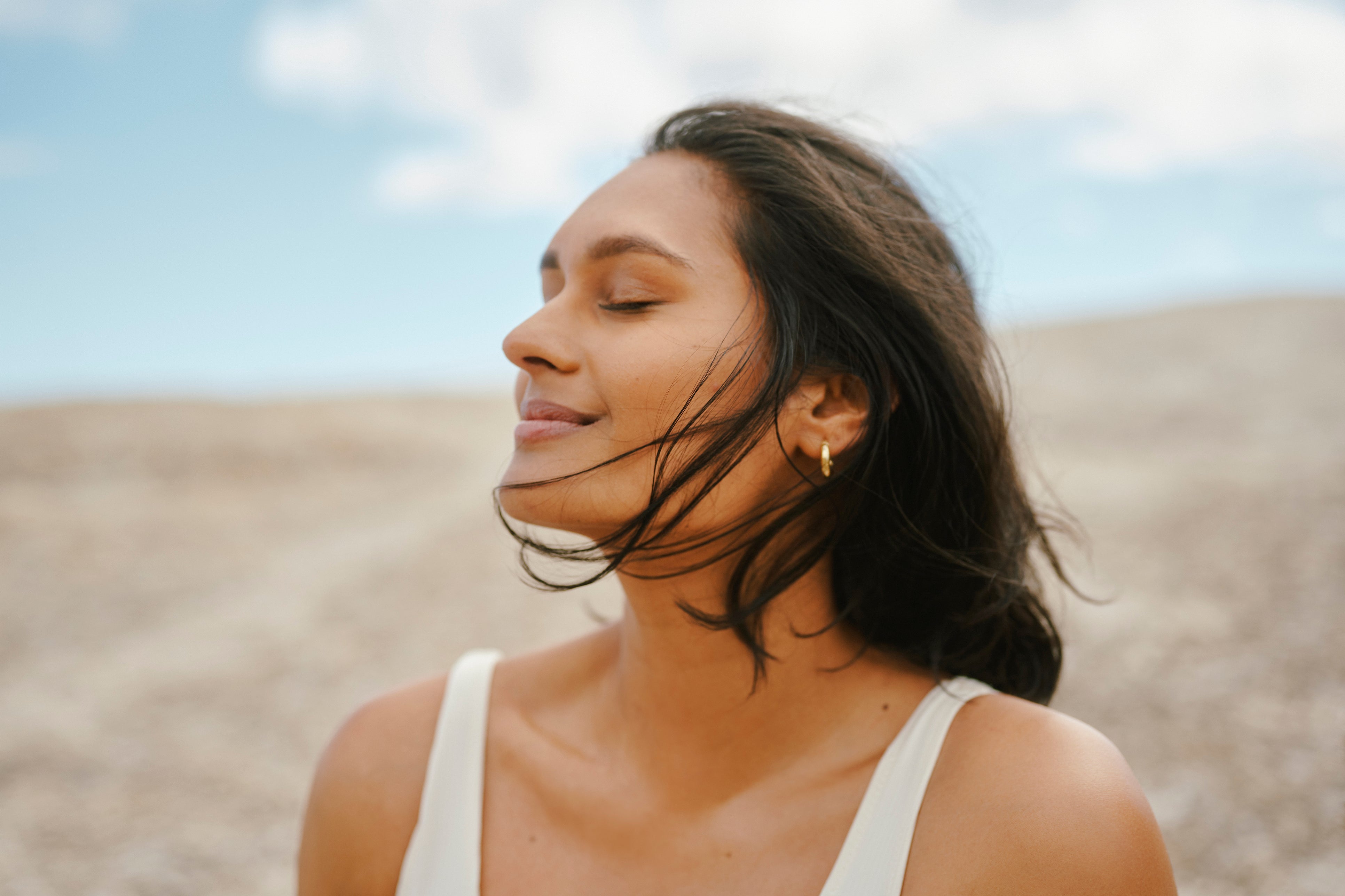 Woman smiling peacefully with eyes closed in a calm outdoor setting